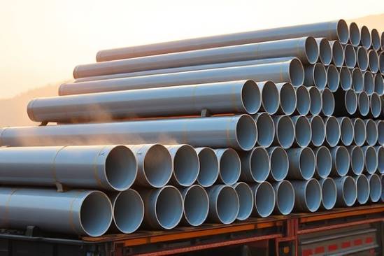 polyethylene pipes, perfectly aligned, waiting for transport, photorealistic, stacked on a flatbed truck, highly detailed, early morning mist rising, golden hour lighting, shot with a telephoto lens.